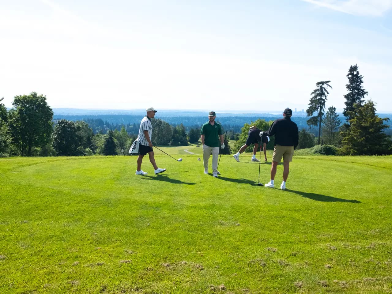 Players spread across a hilltop tee with Puget Sound views beyond