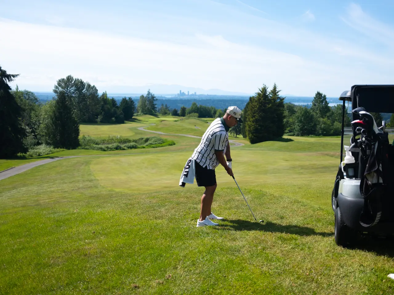 A player set up over the ball beside the cart, city skyline in the distance