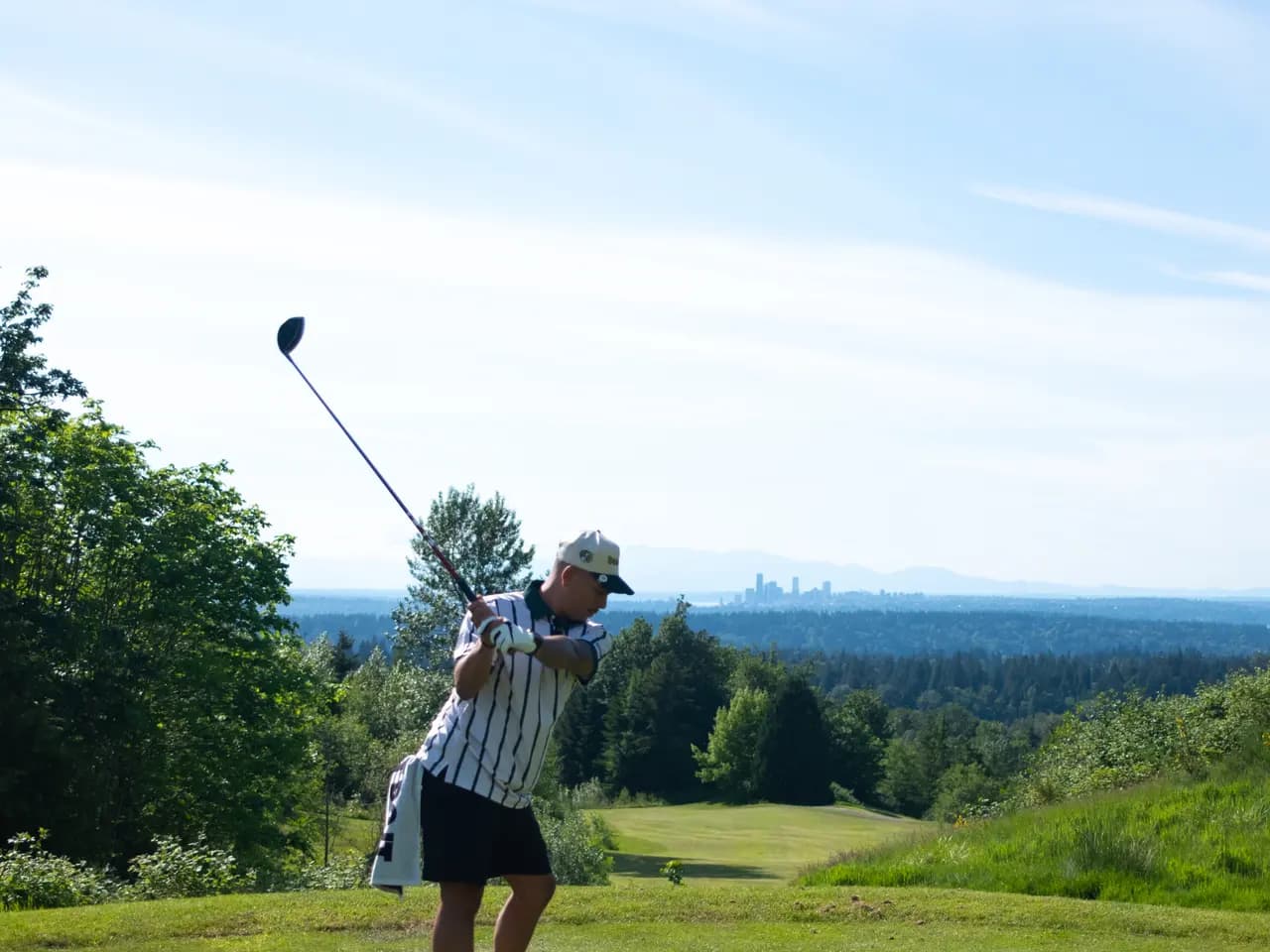 A golfer mid-swing with the Seattle skyline on the horizon