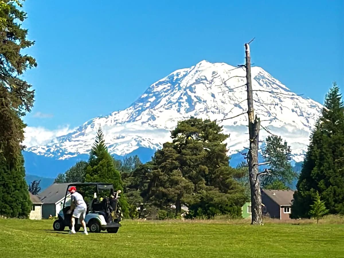 Mount Rainier rising beyond a golfer, cart, and Pacific Northwest fairway