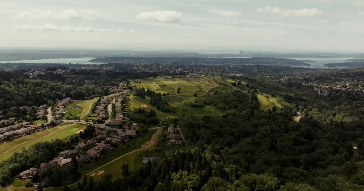 Aerial view of a Washington golf-course neighborhood with Lake Washington and the Seattle skyline beyond.